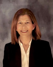 white woman with shoulder length medium brown hair wearing white shirt and black blazer. She's smiling in the picture