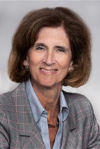 White woman with short brown hair wearing a light blue shirt and gray blazer, smiling