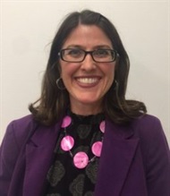 White woman, medium brown shoulder length hair. She's wearing glasses and purple blazer. She's smiling in the picture