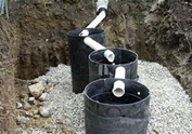 This is a photo of an underground rainwater redirection system with PVC pipes connected through black barrels.