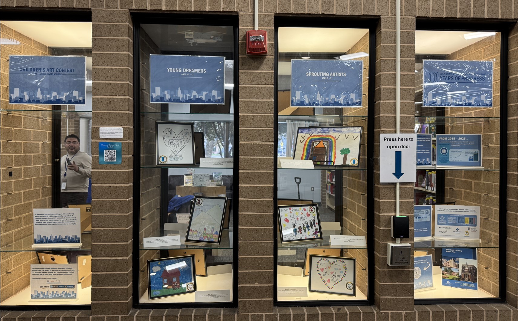 Children's artwork and brief info about affordable housing in Arlington are displayed in glass cases in a brick wall.