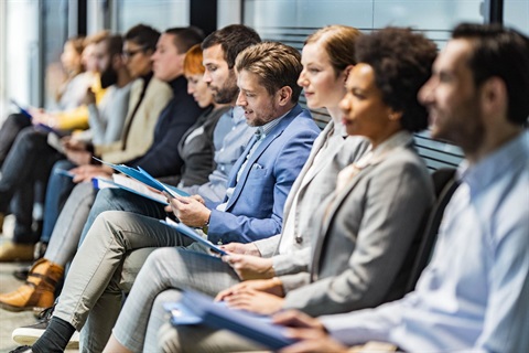 Professionally dressed adults sitting side by side with folders in their hands.